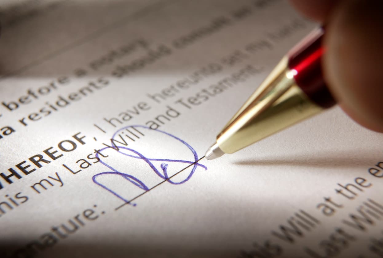 Writing a last will and testament with the help of a professional. Person signing a registered last will and testament in California using a blue pen.