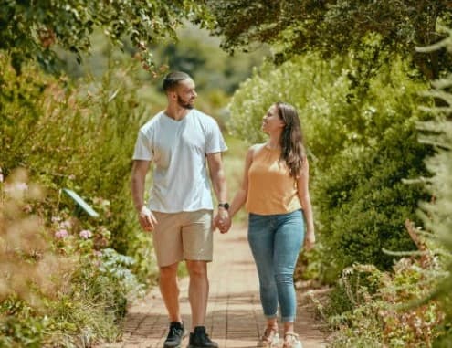 Couple holding hands outdoors wondering how much it costs to create a will Young couple walking outdoors, possibly discussing how much it does cost to create a will for their future.